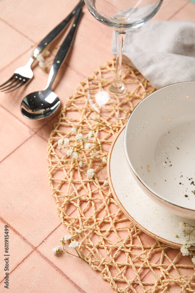 Wicker mat with stylish table setting on pink tile background