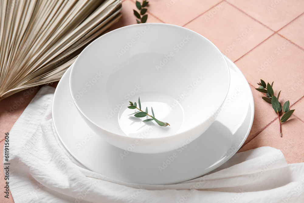 White plates with dry palm leaf on pink tile background