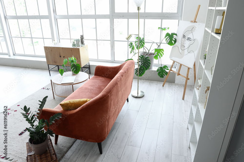 Interior of light living room with cozy brown sofa and coffee table near big window