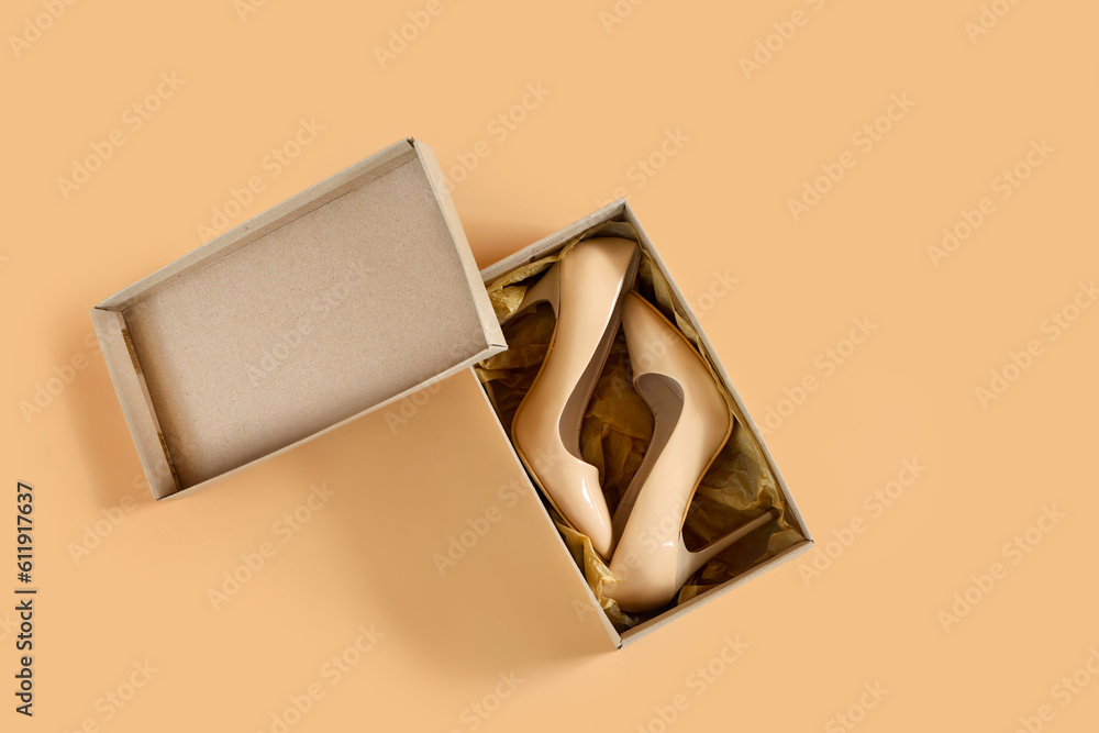 Cardboard box with stylish high-heeled shoes on beige background