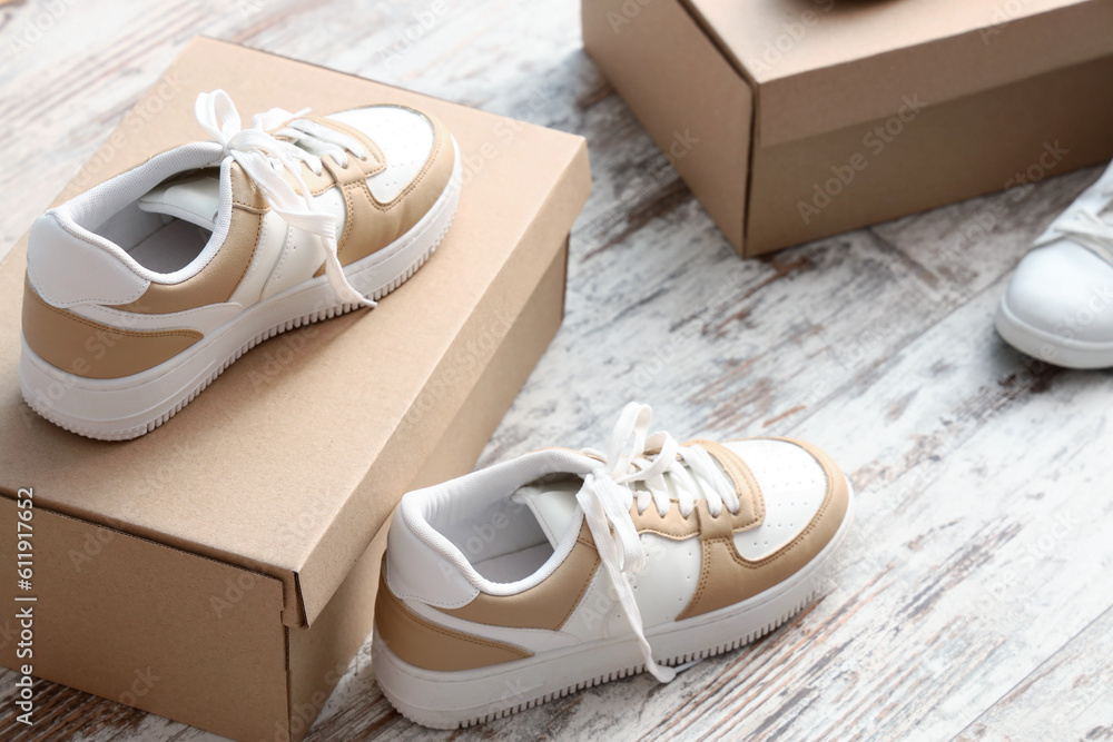 Cardboard boxes with stylish sneakers on light wooden background, closeup