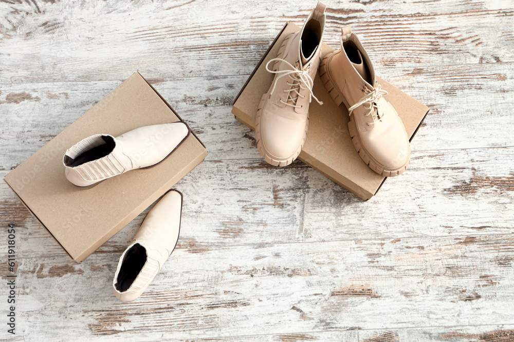 Cardboard boxes with female boots and heeled shoes on light wooden background