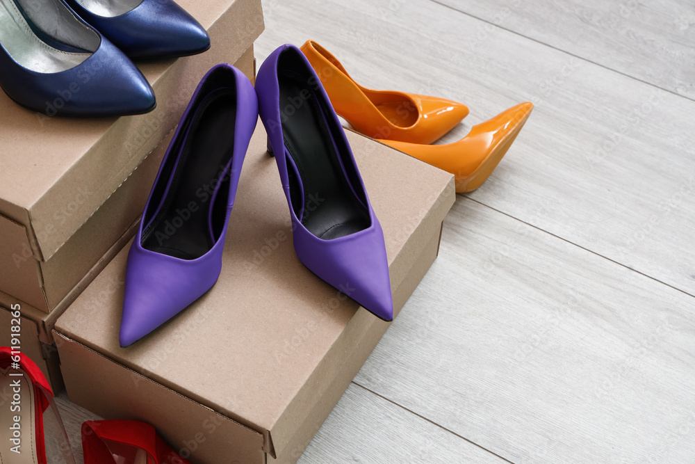 Cardboard boxes with different colorful high-heeled shoes on light wooden background, closeup