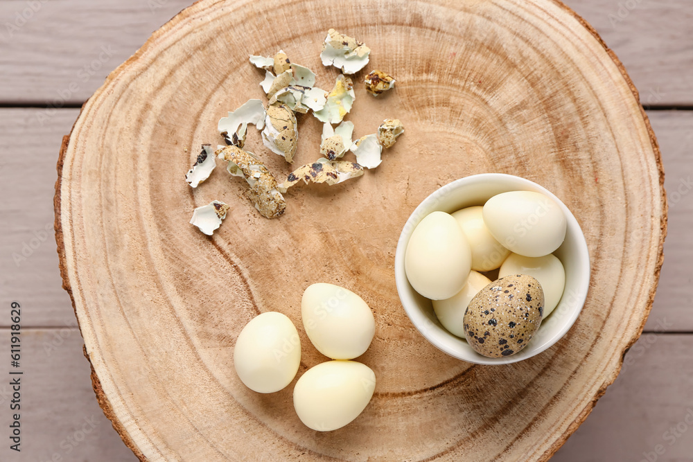 Board with bowl of boiled quail eggs and shells on grey wooden background