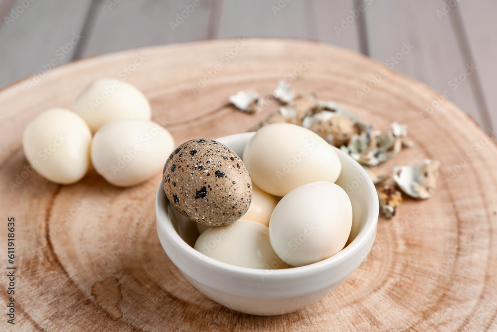 Board with bowl of boiled quail eggs and shells on grey wooden background