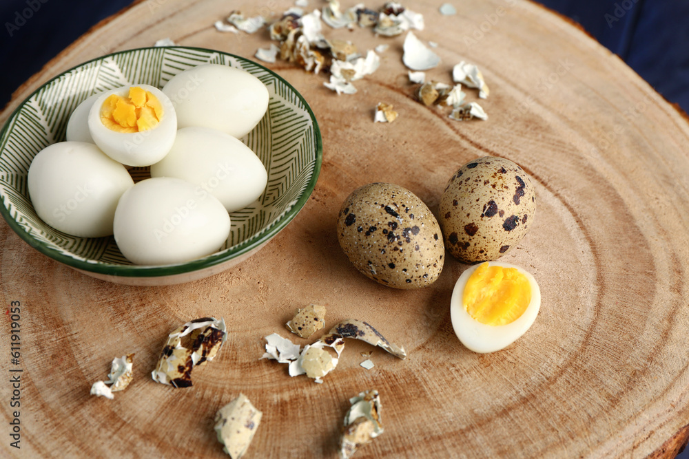 Board with bowl of boiled quail eggs and shells, closeup