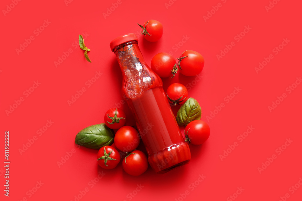 Glass bottle of ketchup and tomatoes on red background