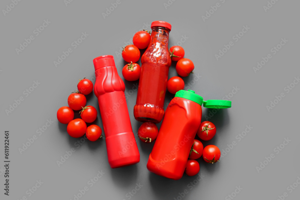 Bottles of ketchup and tomatoes on grey background