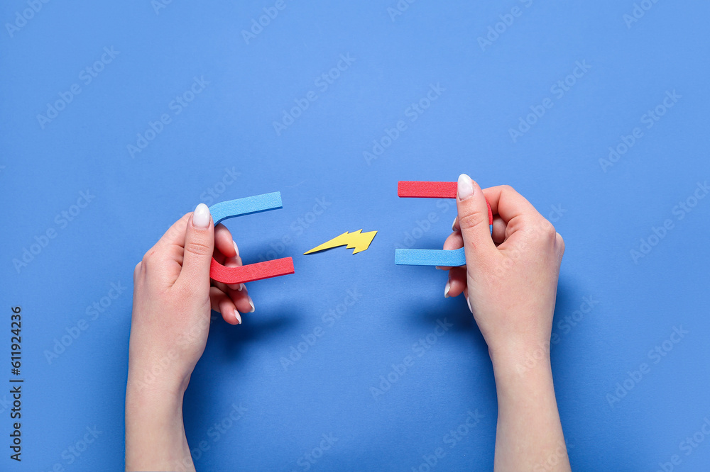 Female hand with mini magnets and paper lightning on blue background