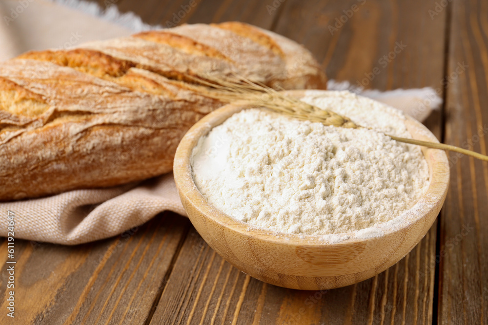 Bowl of wheat flour with fresh bread on brown wooden background