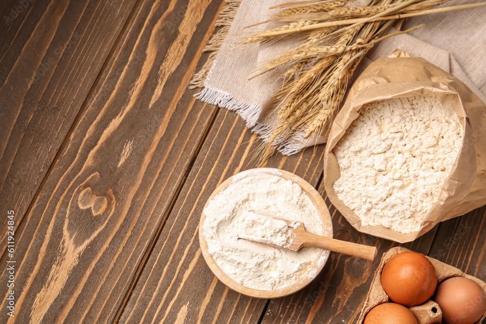 Paper bag with bowl of flour, wheat ears and eggs on brown wooden background