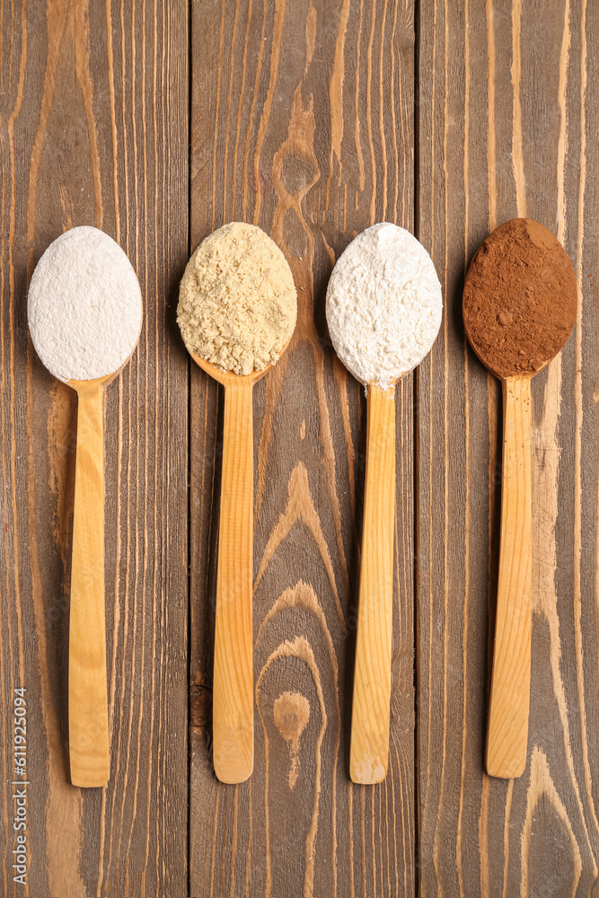 Wooden spoons with different types of flour and cacao on brown wooden background