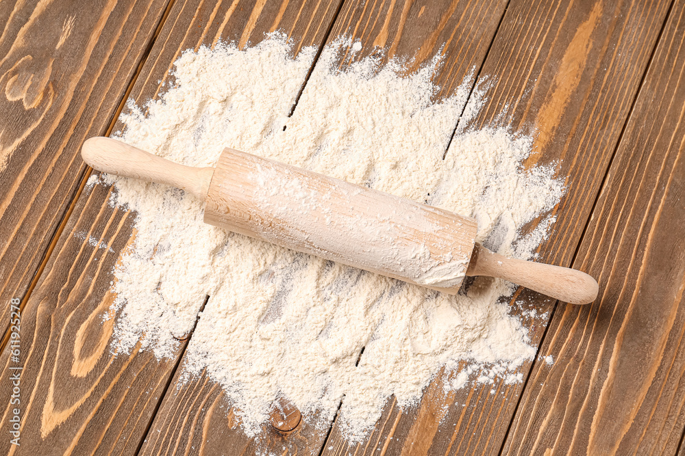 Wooden rolling pin with wheat flour on brown wooden background