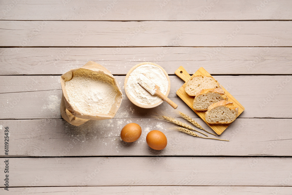 Wooden board with slices of bread, eggs and wheat flour on grey wooden background