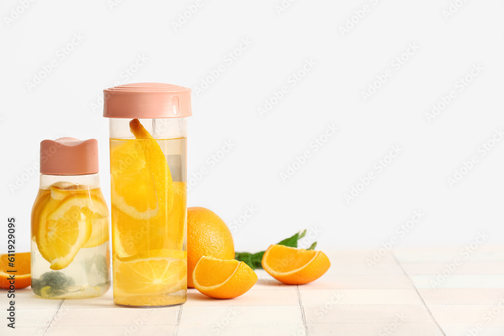 Sports bottles of infused water with orange slices on white tile table