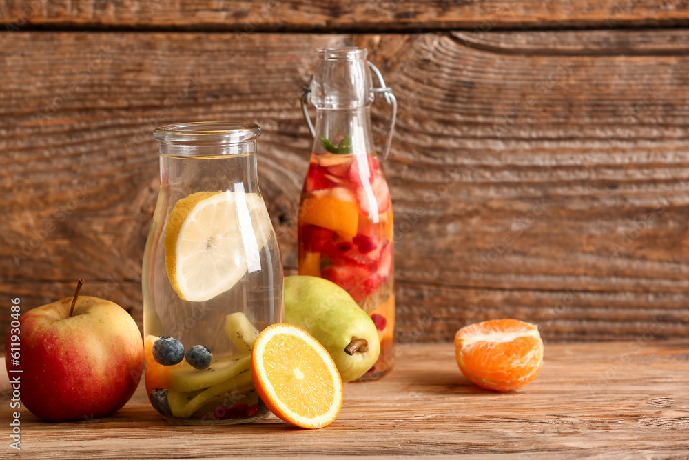 Bottles of infused water with different sliced fruits on wooden table