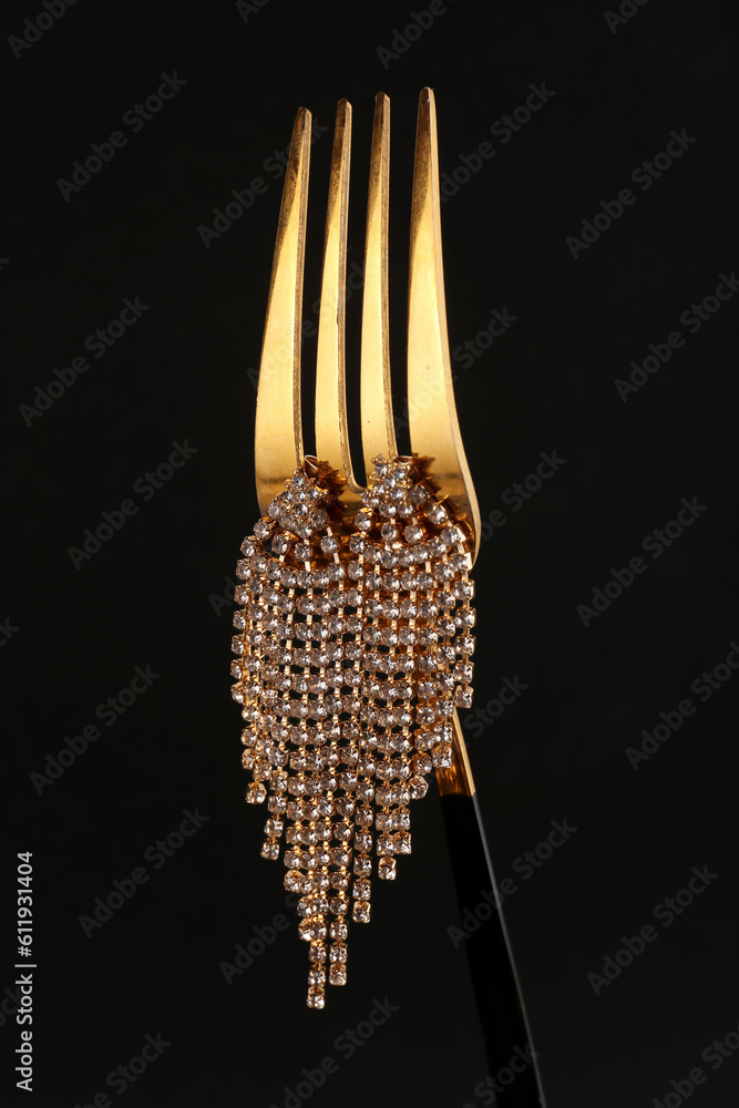 Fork with beautiful earrings on black background