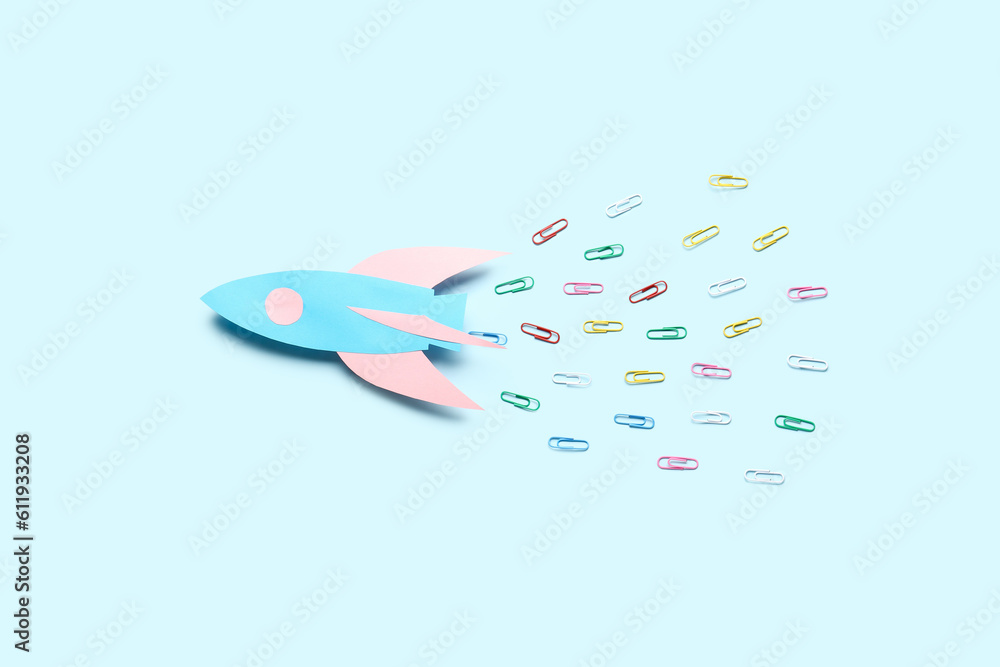 Paper rocket with different colorful paper clips on blue background