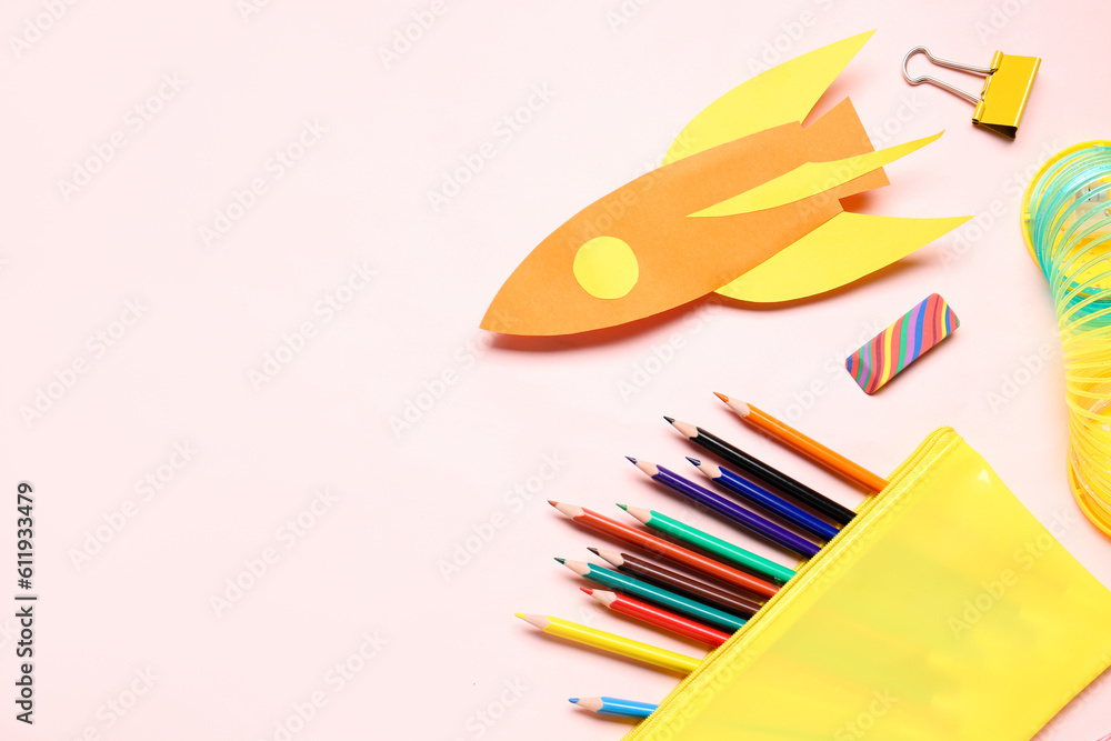 Paper rocket with pencil case and different stationery on pink background