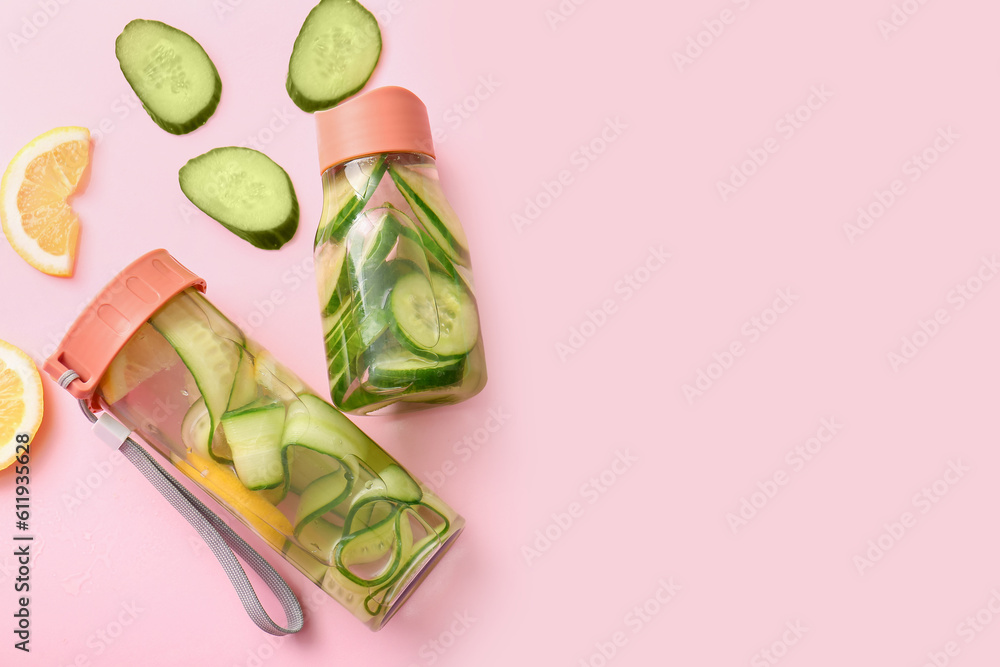 Sports bottles of infused water with cucumber slices on pink background