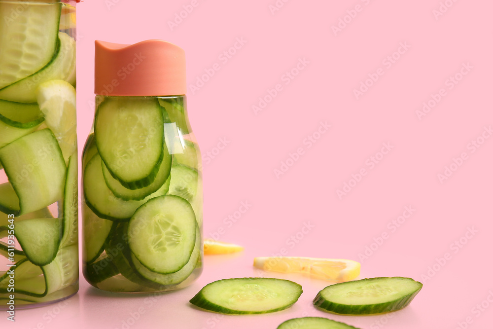 Sports bottles of infused water with cucumber slices on pink background