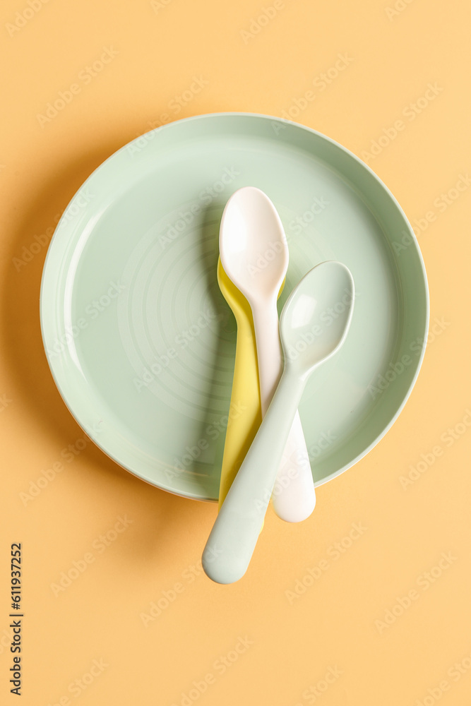 Plate with spoons for baby on pale orange background