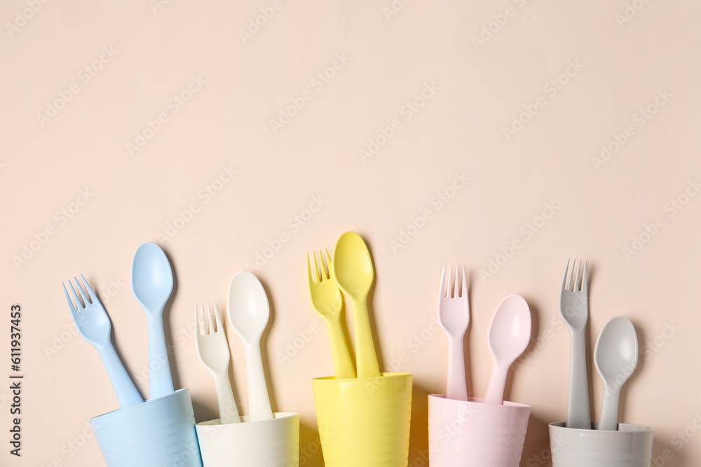 Different cups with cutlery for baby on pale pink background