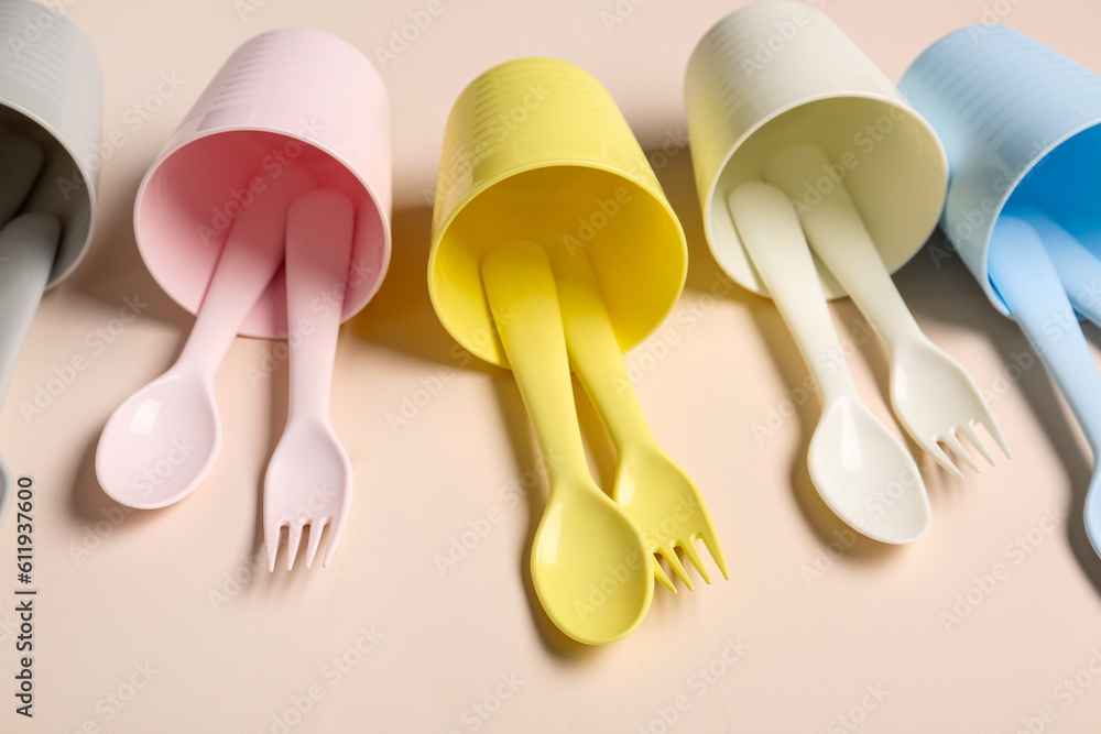 Different cups with cutlery for baby on pale pink background