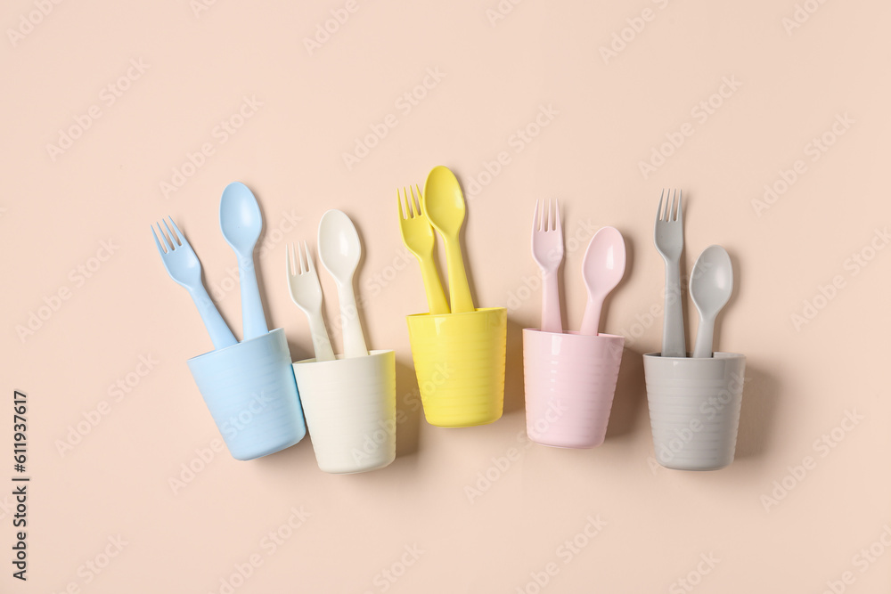 Different cups with cutlery for baby on pale pink background