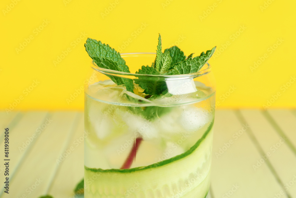 Glass of infused water with cucumber slices on green wooden table