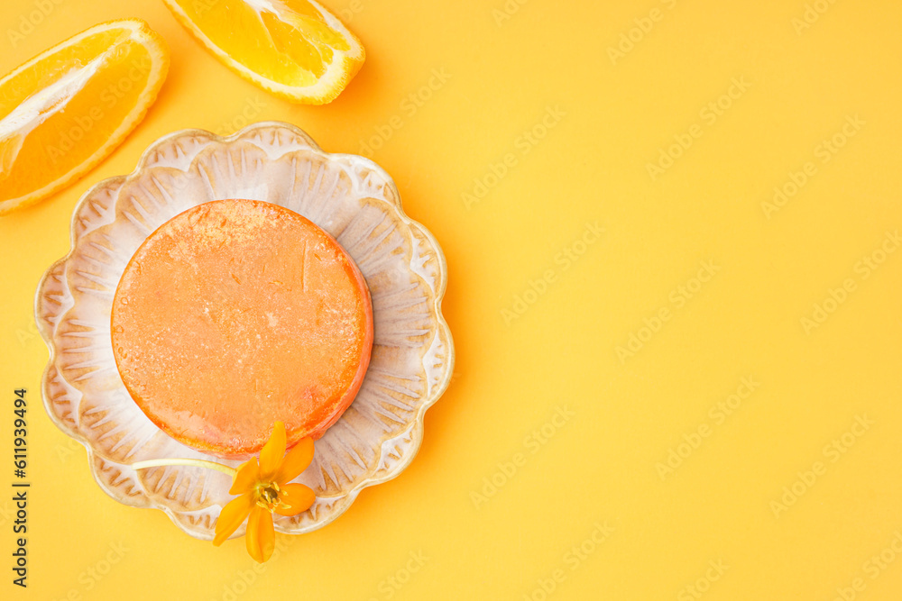 Plate with solid shampoo bar, flower and orange on color background