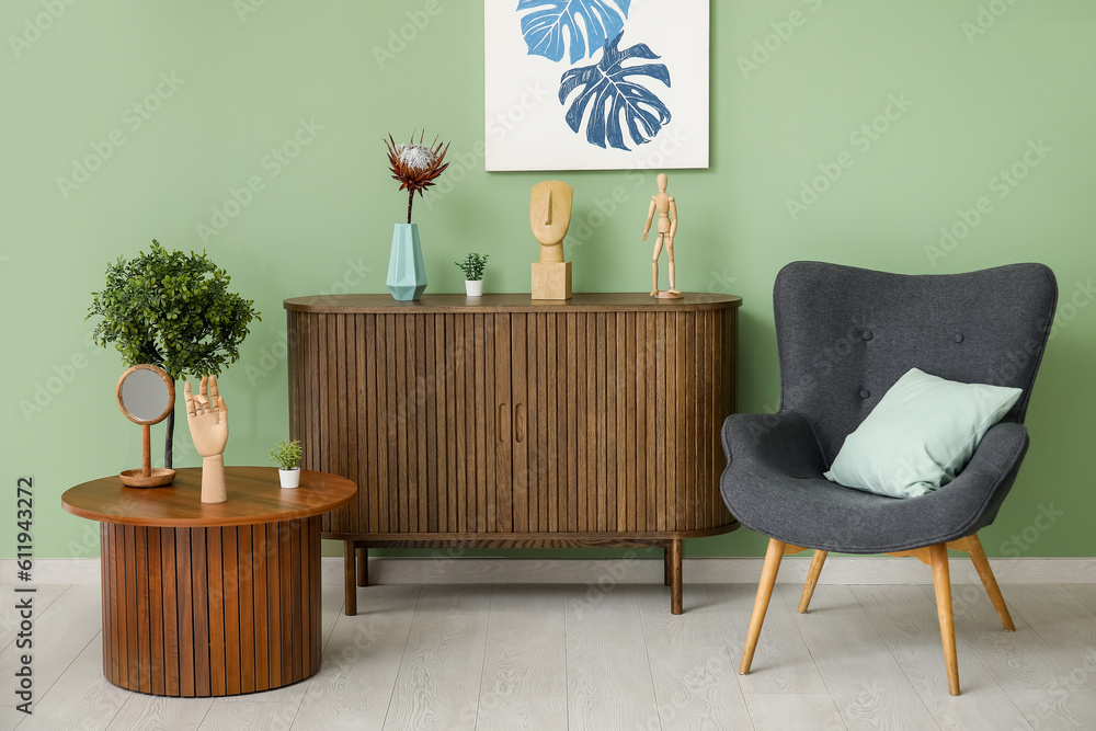 Dark grey armchair with pillow, dresser and coffee table near green wall