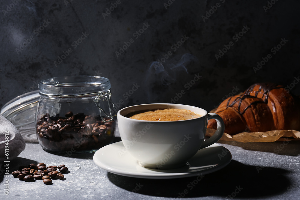 Cup of delicious espresso, coffee beans and croissant on table