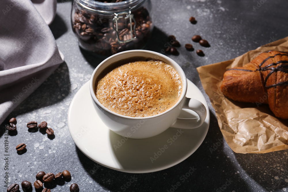 Cup of delicious espresso, coffee beans and croissant on grey background, closeup