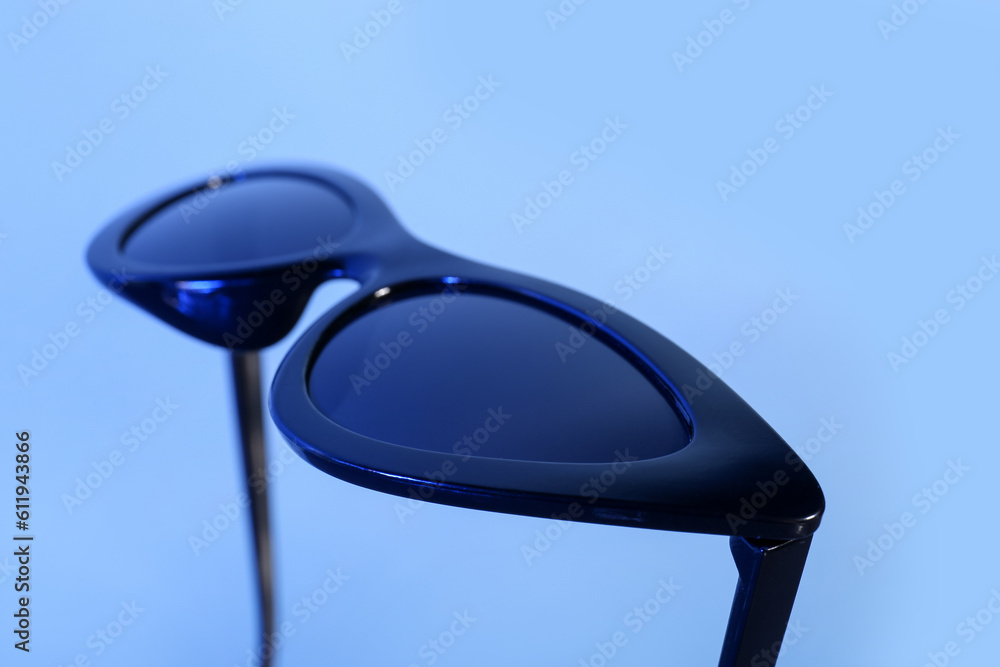 Stylish black sunglasses on blue background, closeup