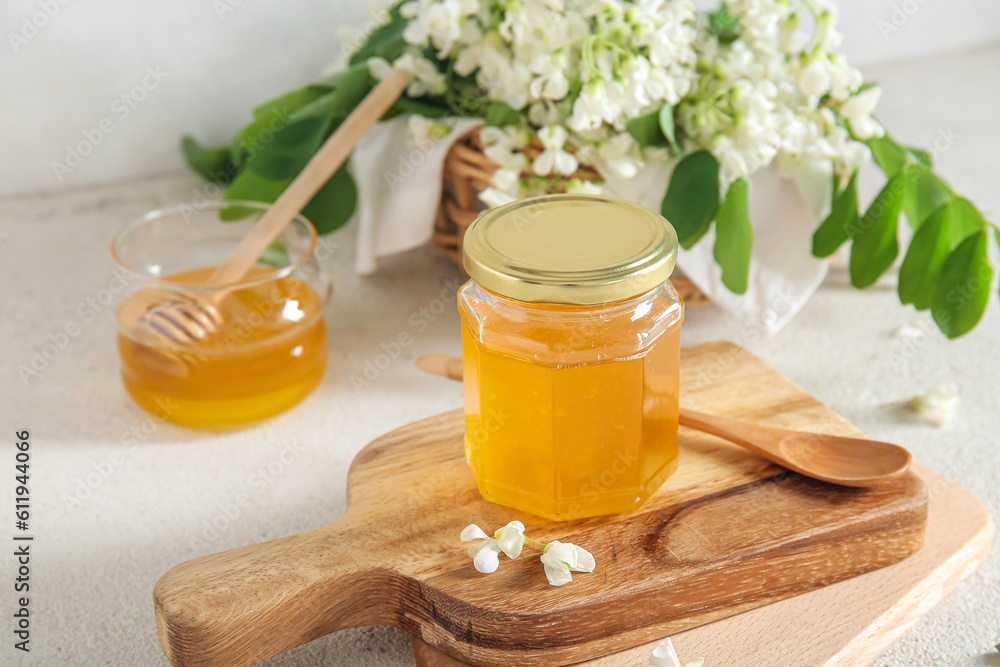 Jar of honey with flowers of acacia on light background, closeup