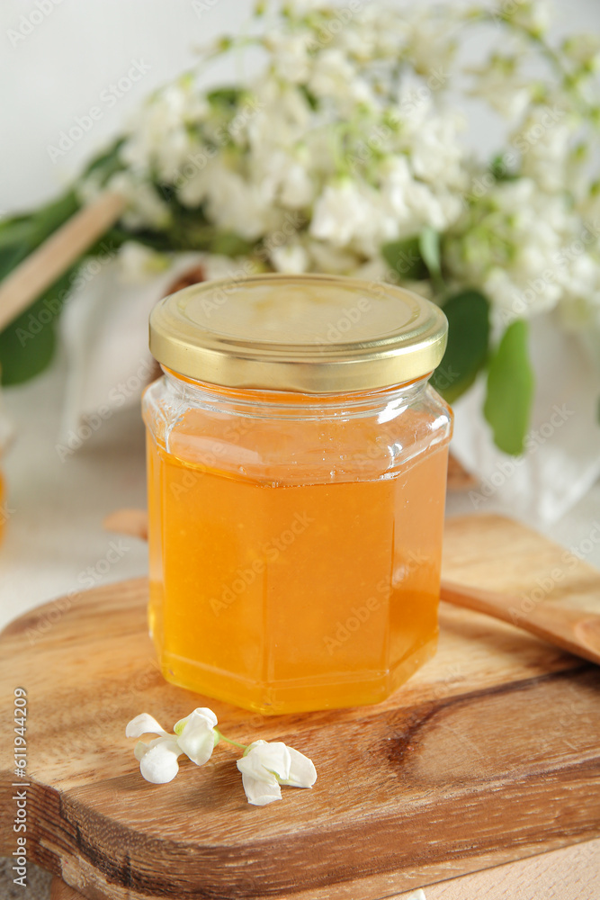 Jar of honey with flowers of acacia on light background, closeup