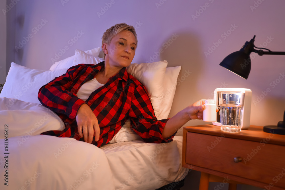 Mature woman with pill bottle in bed at night