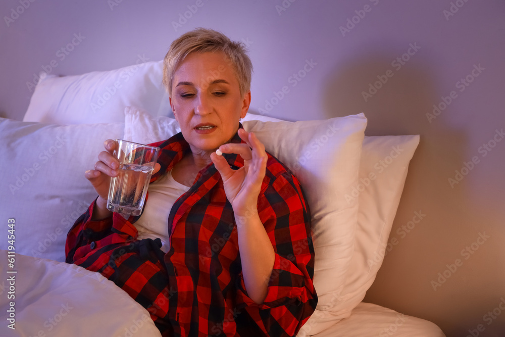 Mature woman with glass of water and pill in bed at night