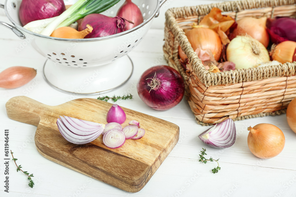 Board, colander and wicker basket with different kinds of onion on white wooden background