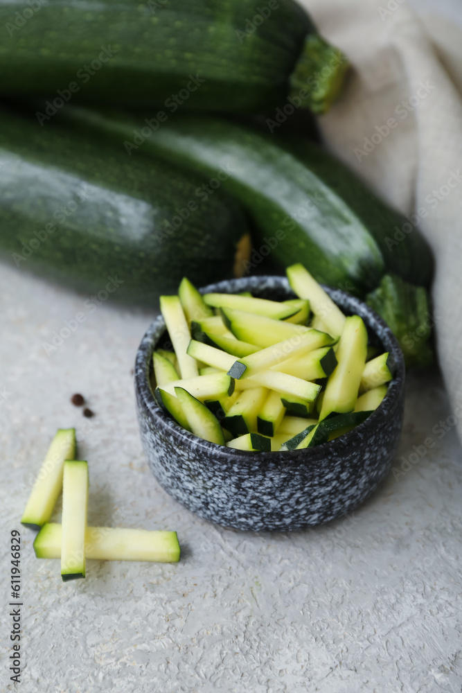 Fresh green zucchini and bowl with slices on grey background