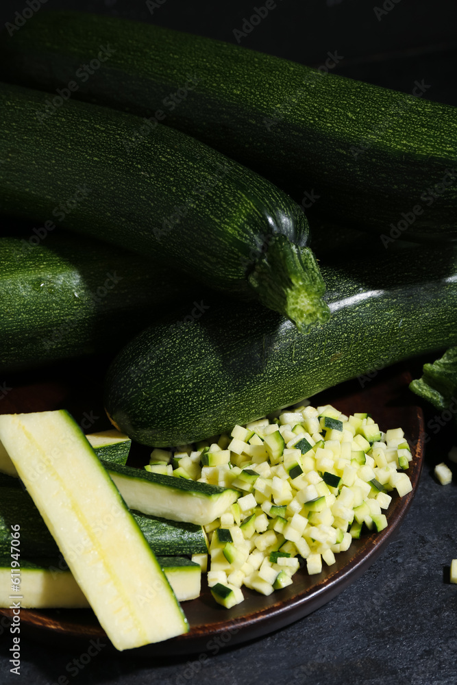 Many fresh zucchini and tray with slices on black table