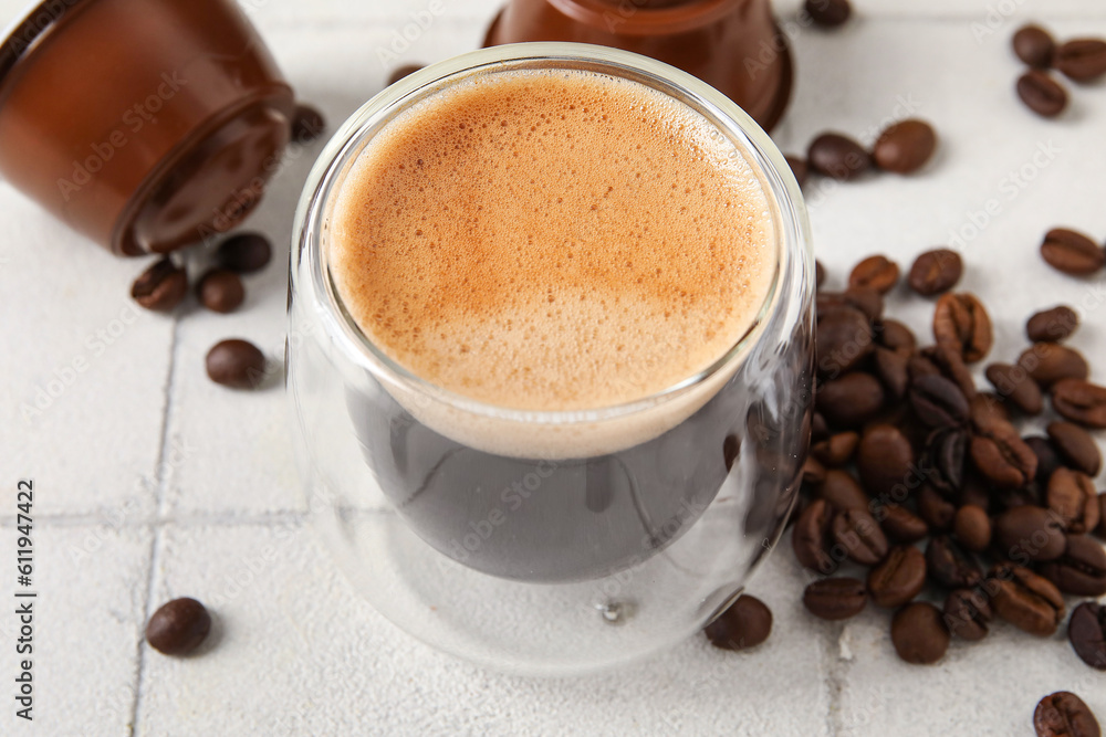 Glass of delicious espresso, pods and beans on white tiled table