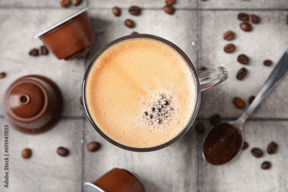 Cup of delicious espresso, pods and beans on grey tiled table