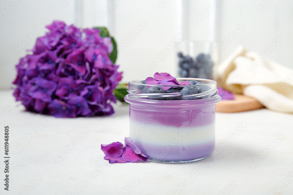 Glass jar of panna cotta with blueberry and beautiful hydrangea flowers on white table