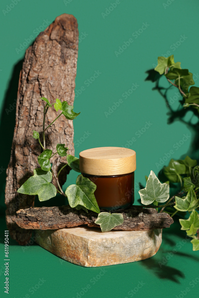 Composition with jar of cosmetic product, tree bark and ivy branch on green background, closeup