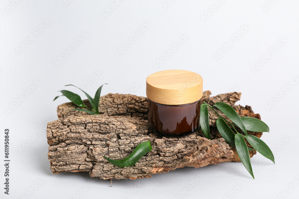 Jar of cosmetic product, tree bark and plant leaves on light background