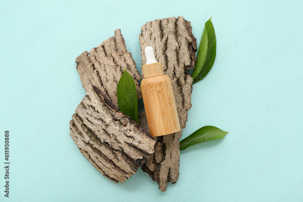 Bottle of essential oil, tree bark and plant leaves on color background