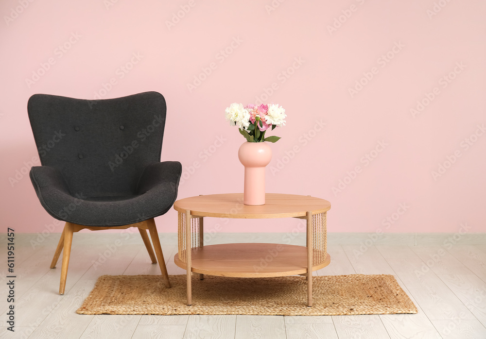 Cozy armchair with wooden coffee table and vase of peonies near pink wall