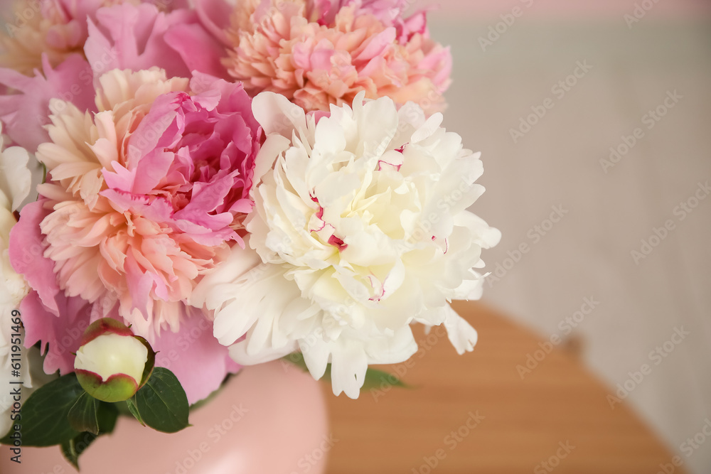 Vase of peonies on wooden coffee table near wall, closeup